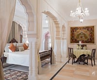 Suite with cusped arches, a curtained bed and a dining table beneath a chandelier