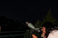 Guest stargazing through a telescope from the verandah at night, valley lights below