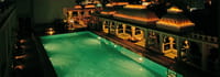 Rooftop swimming pool lit green at night beneath lamp-lined arcades and domed pavilions