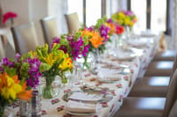 Long banquet table set with colourful lily and orchid arrangements on block-print linen