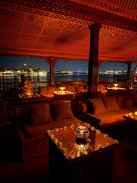 Candle-lit lounge seating aboard the Barge Bahadur at night with city lights across the lake
