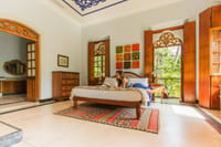 Bedroom with blue ceiling fretwork, carved arched doorways and a guest reading on the bed at Amrapali House of Grace, Goa