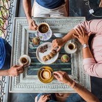 Overhead view of guests having coffee and cookies at a whitewashed table in the cafe at Amrapali House of Grace, Goa