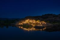 Boulder outcrop lit with lamps beside water at night