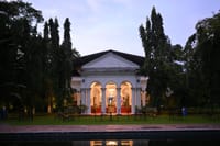 Manor facade lit at dusk seen across the pool