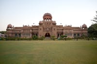 Red sandstone palace facade with domes and lawns at dusk
