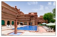 Outdoor swimming pool with sun loungers against the carved sandstone palace wings