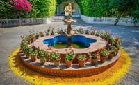 Garden fountain ringed with potted flowers and rangoli