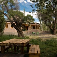 Chulli Bagh villa exterior with stone base, timber-framed windows and picnic benches under apricot trees at Stok Palace Heritage, Leh