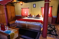 Heritage Room Without Balcony with pale wooden bed, dark canopy and yellow ochre walls at Stok Palace Heritage, Leh