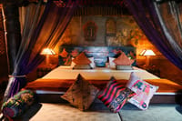 Queen's Room canopied bed with silk drapes, painted headboard and mural-covered walls at Stok Palace Heritage, Leh