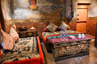 Queen's Room sitting area with carpeted day beds, carved dragon chest and old painted walls at Stok Palace Heritage, Leh