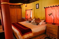 The Royal Suite bed with red canopy pillars, fleece-trimmed throw and orange curtains at Stok Palace Heritage, Leh