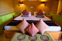 The Royal Suite bed with cushions and bolsters against green cane wainscoting and ochre walls at Stok Palace Heritage, Leh