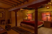 The Royal Suite interior with carved red canopy columns, wooden wardrobes and Tibetan rugs at Stok Palace Heritage, Leh