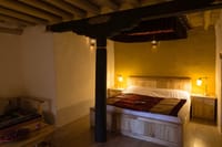 Standard Suite room seen through carved painted beams, with black-covered bed and Ladakhi rugs at Stok Palace Heritage, Leh