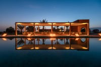 Poolside pavilion lit up at dusk, reflected in the still pool