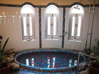 Round mosaic tiled sunken bath below arched windows