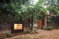 Brick entrance gate with the Mela Kothi lodge sign among trees