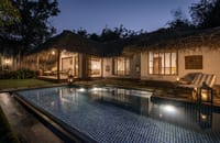 The swimming pool and thatched villas lit at night