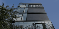 Black glass-and-steel exterior of NUO with the hotel logotype against a blue sky