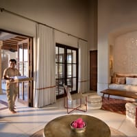Kothi living room with cushioned seating nook, hammered brass table and staff member bringing towels at Aramness, Sasan Gir