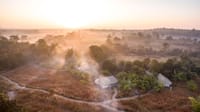 Aerial view of tented camp roofs among trees and grassland in dawn mist at Jamtara Wilderness Camp, Pench