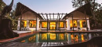 Main lodge lit at dusk with its reflection in the pool and bicycles parked on the deck at Jamtara Wilderness Camp, Pench