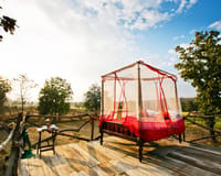 Star Bed — four-poster bed with mosquito net and morning tea on an open wooden deck over the fields at Jamtara Wilderness Camp, Pench
