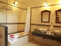 Bathroom with bathtub, twin basins on a granite counter and carved wooden mirrors at Irai Safari Retreat, Tadoba