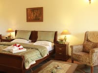 Bedroom with wooden bed, patterned green quilt, bedside lamps and leopard-print armchair at Irai Safari Retreat, Tadoba