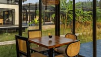 Cane dining chairs and table in the glass-walled Den restaurant looking onto banana plants at Bori Safari Lodge, Satpura
