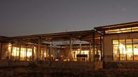Lodge buildings lit up at dusk with glass walls glowing over the grassland at Bori Safari Lodge, Satpura