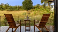Luxury Room — two wooden chairs and wine on the private deck facing tall grass at Bori Safari Lodge, Satpura