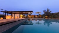 Tiled swimming pool at dusk with lanterns, umbrellas and the lodge behind at Bori Safari Lodge, Satpura