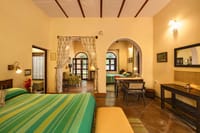 Bedroom with green striped bedspread opening through arches to a sitting area and second room at Mela Kothi – Chambal Safari Lodge, Chambal