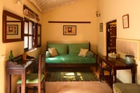 Cottage sitting area with green cushioned daybed, writing desk and wooden shuttered window at Mela Kothi – Chambal Safari Lodge, Chambal