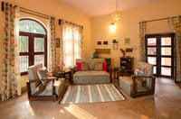 Sitting room with paisley upholstered sofa and armchairs, floral curtains and arched windows at Mela Kothi – Chambal Safari Lodge, Chambal