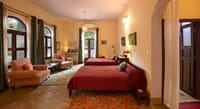 Bedroom with two beds in red striped covers, armchairs and arched windows at Mela Kothi – Chambal Safari Lodge, Chambal
