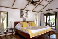 Jungle Lodge bedroom at Jim's Jungle Retreat with yellow and white bedding and doors opening onto a private balcony