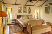 Jungle Lodge bedroom at Jim's Jungle Retreat with a wooden double bed under a bamboo-framed ceiling, cane sofa with tiger-print cushions and a ceiling fan