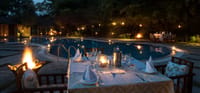 Candlelit dinner table beside the swimming pool at dusk with fire braziers at Jim's Jungle Retreat, Corbett