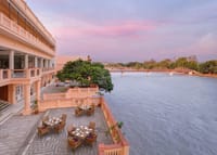 Riverside terrace with dining tables overlooking the Ganges and a bridge at sunset at Pilibhit House, Haridwar