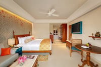 Premium Room Ganges View at Pilibhit House with a carved wooden king bed, teal-framed wall TV, round wooden table and a sofa with orange cushions