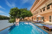 Mosaic-tiled swimming pool beside the Ganges under a mango tree with striped sun loungers at Pilibhit House, Haridwar