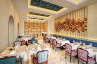 The Dining Room restaurant with floral upholstered chairs, blue banquette and painted ceiling panels at Pilibhit House, Haridwar