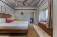 Arundhati suite bedroom with upholstered headboard, armchairs and floor lamp by the window at Amrit Bhawan, Haridwar