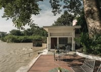 Riverside terrace and private ghat beside the flowing Ganga, shaded by a large tree, at Amrit Bhawan, Haridwar