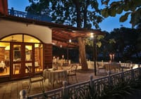 Candlelit tables on the Jaagir Pavillion restaurant terrace beneath a tree at dusk at Jaagir Manor, Dudhwa