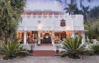 White art deco manor facade framed by palms and ferns at dusk at Jaagir Manor, Dudhwa